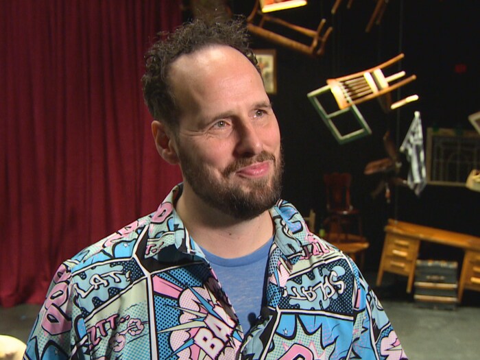 Portrait de Simon Miron, metteur en sc&egrave;ne, sur la sc&egrave;ne du Th&eacute;&acirc;tre Cercle Moli&egrave;re, entour&eacute; d&rsquo;&eacute;l&eacute;ments de d&eacute;cor suspendus.