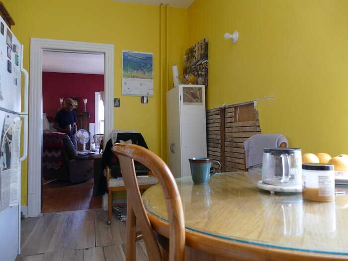 Une petite cuisine peinte en jaune vif avec un trou dans le mur qui laisse voir des lattes de bois.
