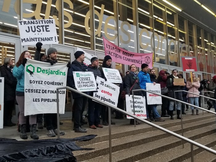 Des manifestants environnementalistes devant le Palais des congrès de Montréal tiennent des affiches.