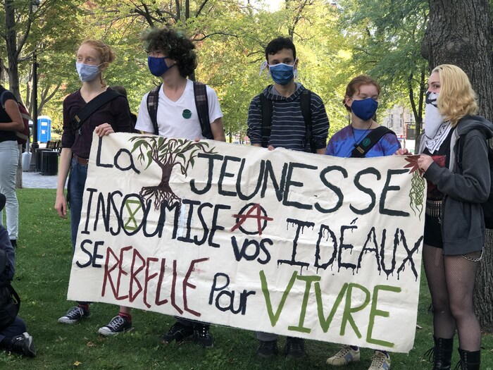 Des jeunes portant des masques et une affiche sur laquelle on peut lire « La jeunesse insoumise à vos idéaux se rebelle pour vivre ». 