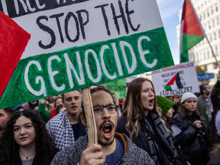 Un homme tient une pancarte aux couleurs du drapeau palestinien sur laquelle il est écrit : Arrêtez le génocide.