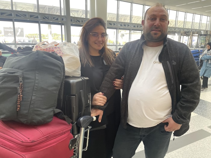 Une femme tient le bras d'un homme devant un chariot de bagages.