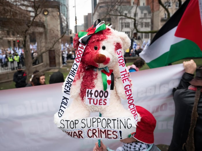 Une personne tient un bâton sur lequel se trouve une peluche ensanglantée sur laquelle se trouvent des drapeaux palestiniens.
