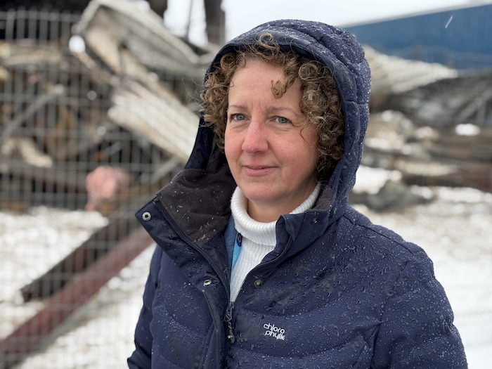 Une femme sourit à la caméra. Un monticule de débris est visible derrière.