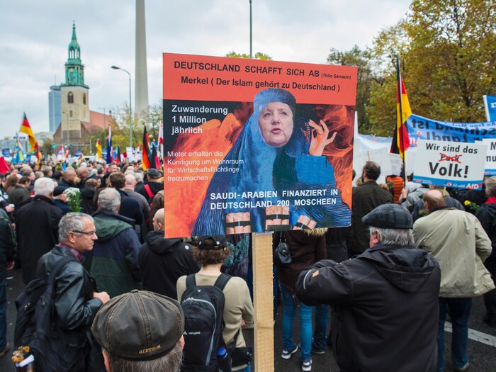 Des manifestants tiennent des pancartes, dont une avec le visage d'Angela Merkel plaqué sur une burqa.