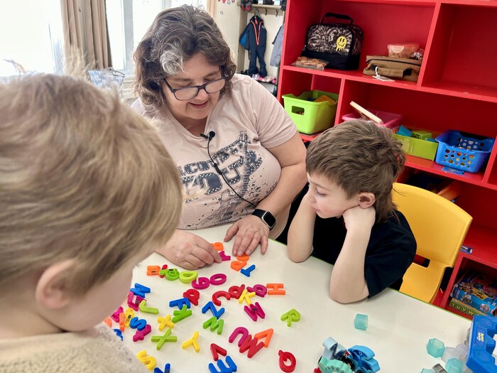 L'éducatrice Micheline Leblanc aide des enfants à trouver des lettres de l'alphabet disposées sur une table.