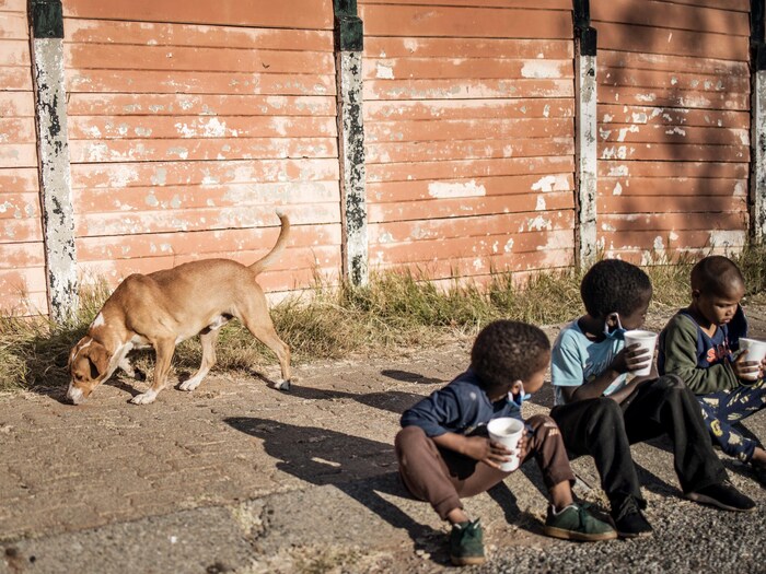 Trois enfants mangent, assis sur le trottoir.