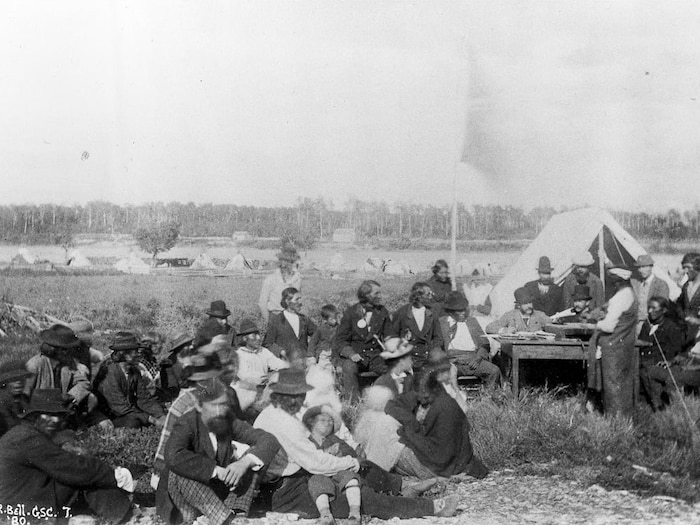 Des personnes sont assises dans l'herbe. Au loin on aperçoit des habitations. Photographie d'archives de St. Peters en 1880. 