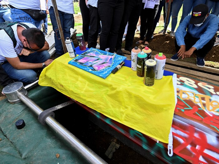 Deux hommes sont agenouillés devant un cercueil couvert de tags.