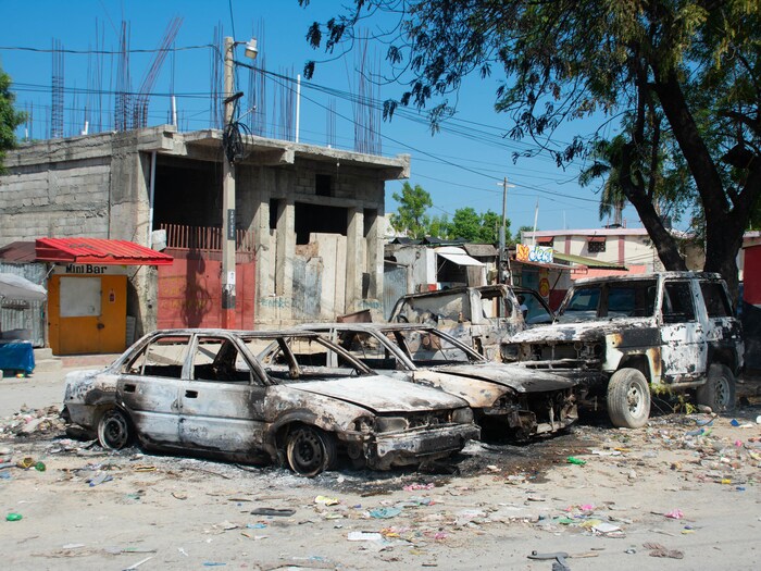 Des voitures incendiées dans une rue déserte de Port-au-Prince, jonchée de déchets.