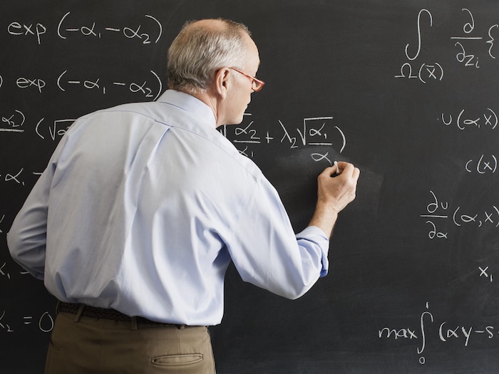 Un professeur écrit une équation d'algèbre au tableau.