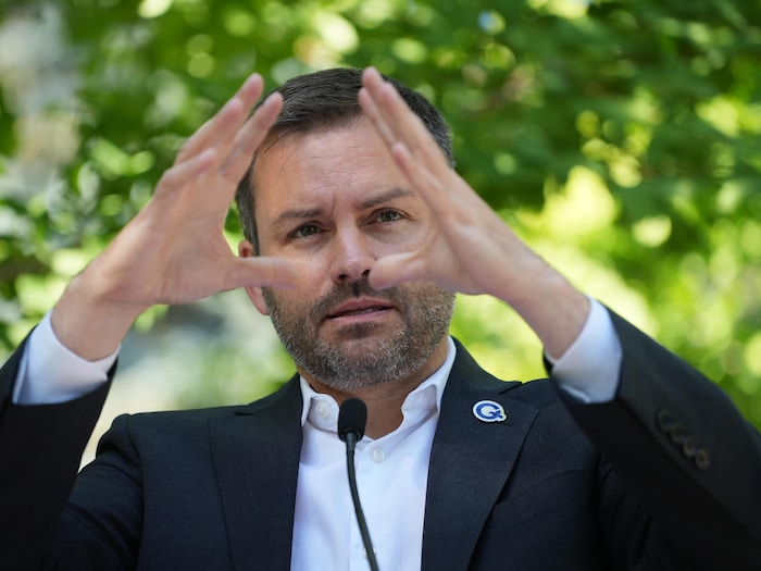 Paul St-Pierre Plamondon fait un symbole de pyramide avec ses mains en parlant à un micro.
