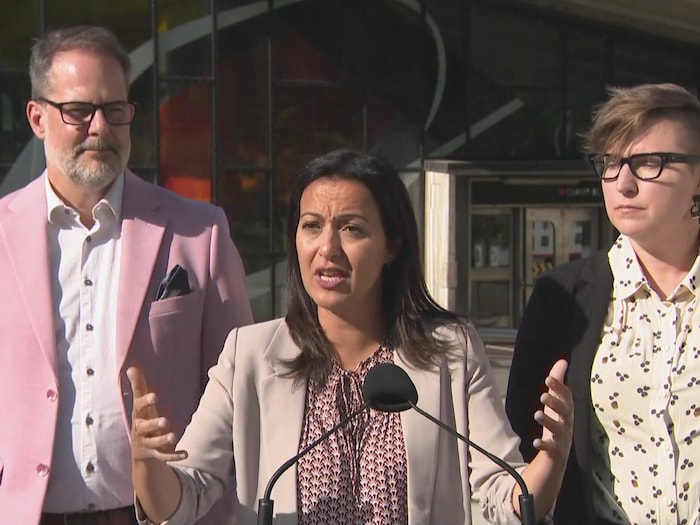 Ruba Ghazal parle en gesticulant derrière un podium muni d'un micro, en dehors de l'édicule d'une station de métro.