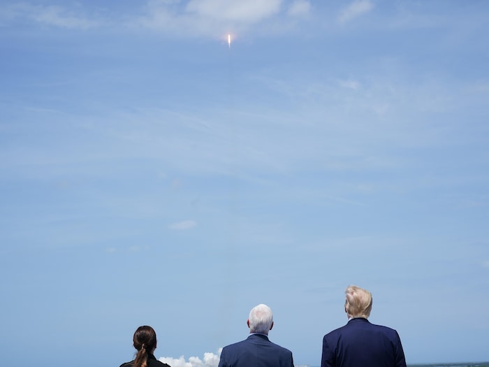 Mike Pence et Donald Trump, de dos, regardant vers un ciel bleu dégagé une fusée s'élevant vers l'espace.