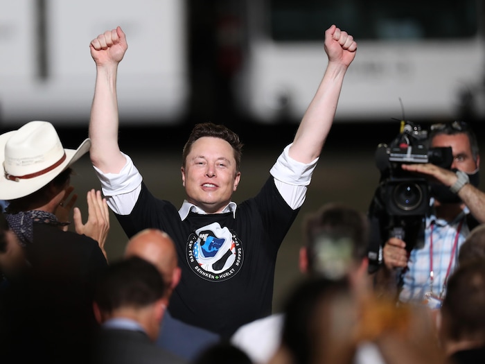 Elon Musk lève les bras dans les airs, heureux, entouré de personnes.