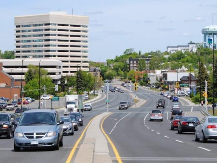 Une rue du centre-ville de Sudbury. Les voitures sont en mouvement. Au loin, le château d'eau de Sudbury.