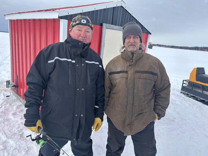 Roméo Butch Boudreau et Roger Blanchard debout devant une cabane à éperlans.
