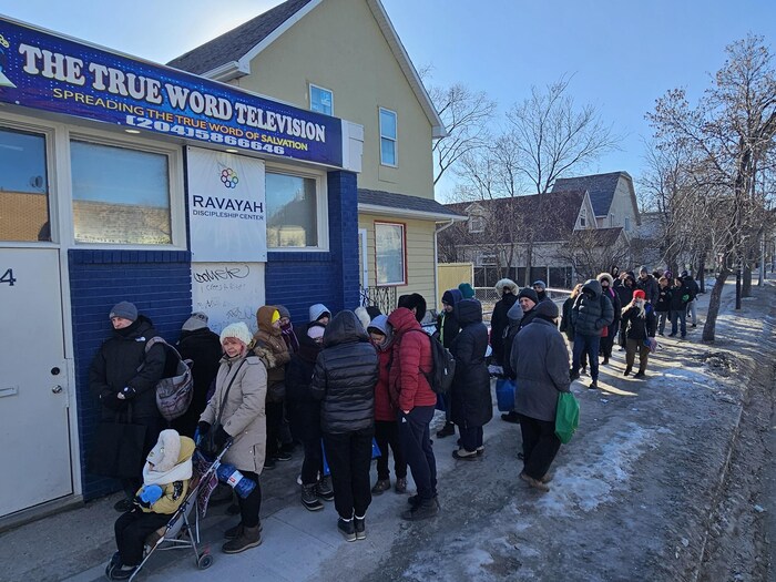 Des gens font la queue devant les locaux de True Word TV, à Winnipeg, pour une distribution de denrées alimentaires.