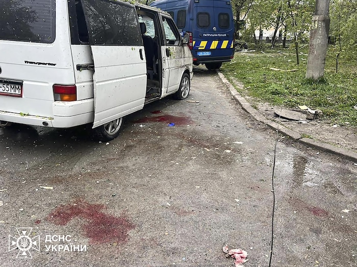 Sur le sol, à côté d'une camionnette garée dans une rue, des taches de sang sont visibles sur l'asphalte. 