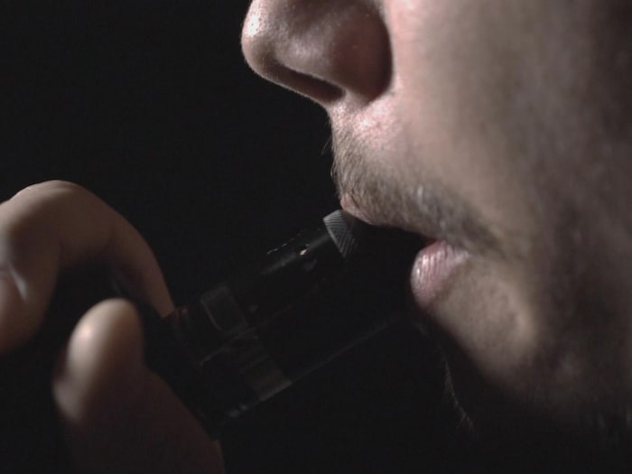 Gros plan sur la bouche et les doigts d'un homme qui vapote.