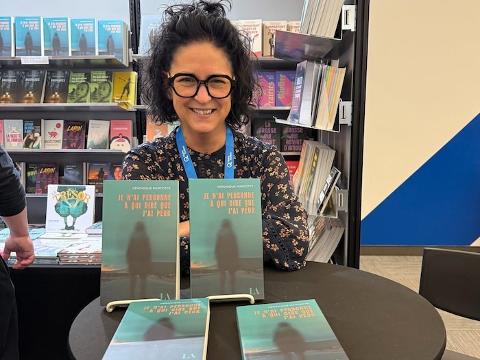 Une femme brune pose à côté de livres. 