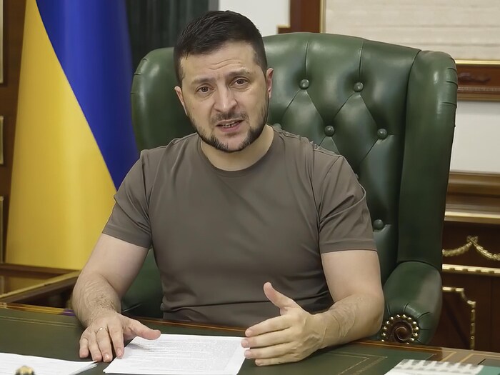 Vêtu d'un t-shirt kaki, Volodymyr Zelensky est assis sur un fauteuil vert derrière son bureau.