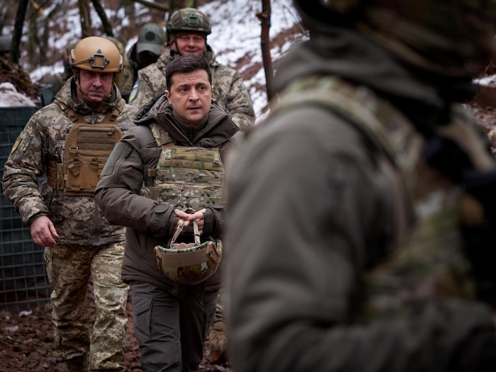 En habit de combat, Volodymyr Zelensky marche dans un boisé enneigé avec des soldats.