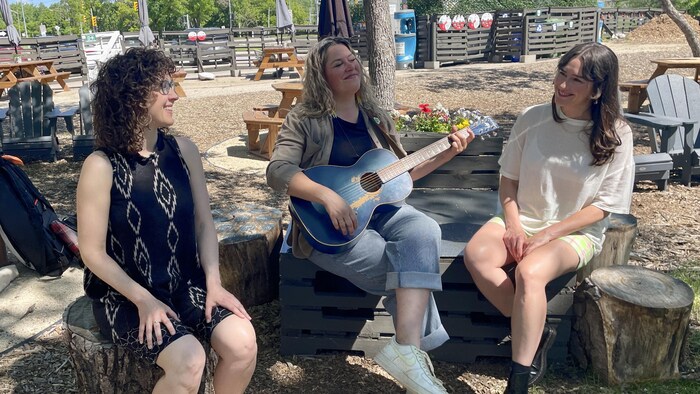 Trois jeunes femmes assises en train de chanter et de jouer de la guitare.