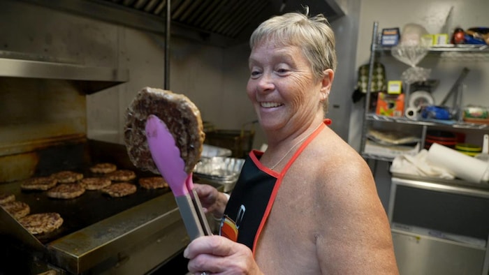Kim Stevens prépare des hamburgers sur le gril en tenant une galette de viande avec une pince.