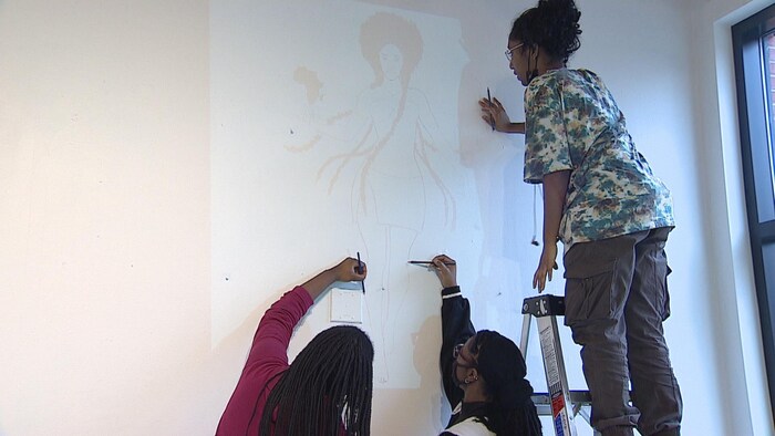 Les trois élèves peignent une image sur le mur blanc.