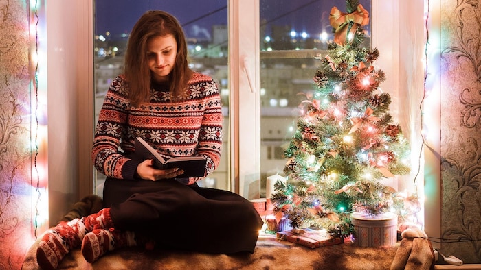 Une jeune femme lit un roman dans un décor de Noël. 