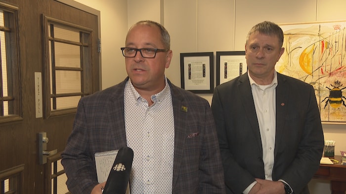Éric Marquis et Philippe Landry, debout, répondent aux questions des journalistes dans un couloir.