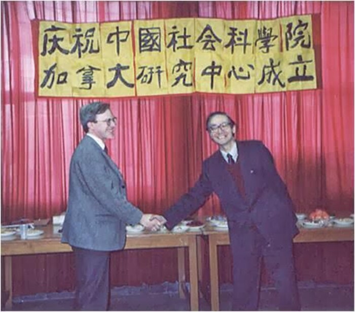 兩個人握手。 在他們上方，一張海報上寫著“中國慶祝社會科學院加拿大研究中心成立”