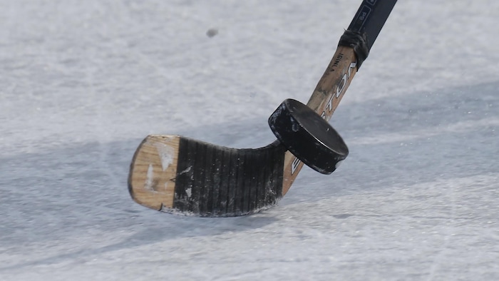 Un bâton de hockey qui frappe une rondelle sur une patinoire.