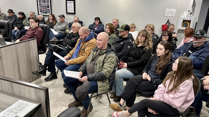 Des citoyens sont assis dans une salle du conseil municipal de Belle-Baie.