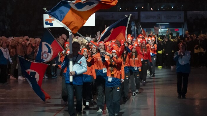 Un cortège de jeunes sportifs portant la pancarte de leur région et des drapeaux.