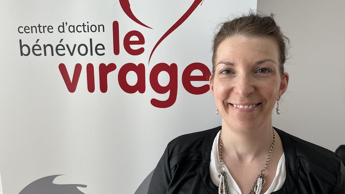 Karoline Gilbert est devant une affiche du Centre d'action bénévole Le Virage de Sept-Îles.