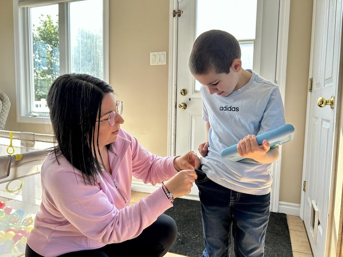 Karine Robichaud est en compagnie de son fils Anthony. Elle est sur le point d'accrocher l'appareil AngelSense sur le pantalon de son fils.