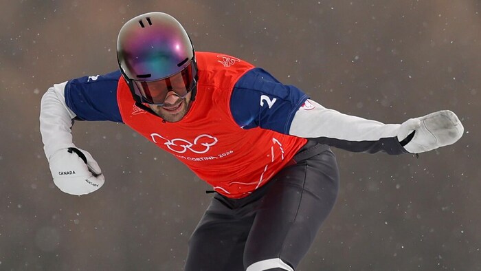 Sur sa planche, Éliot Grondin vole dans les airs lors de la compétition de snowboard cross.