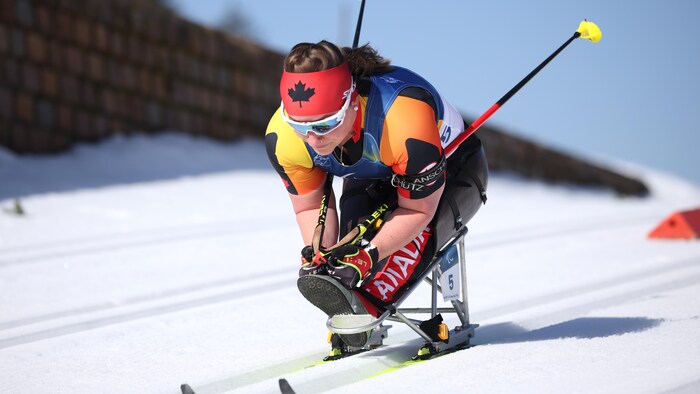 Une parabiathlonienne est penché, les skis sous ses bras pour aller plus vite.