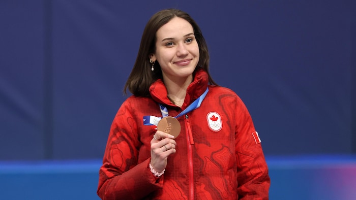 Elle sourit et tient sa médaille dans sa main droite.