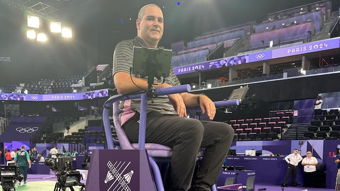 Éric Desroches at the top of a raised chair on the edge of a badminton field.