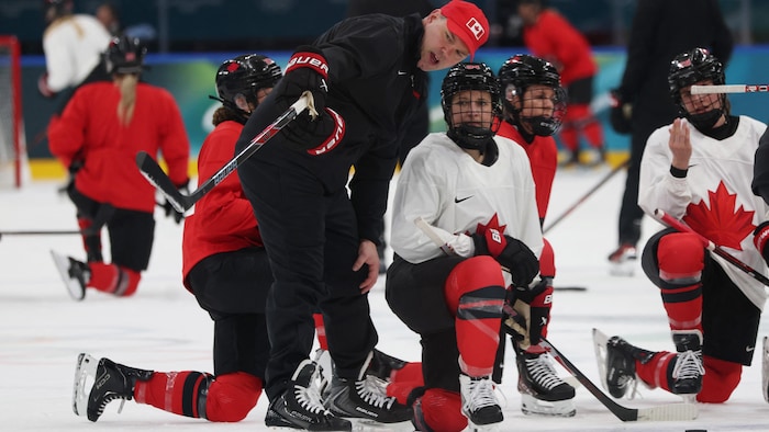 Il pointe un endroit sur la glace avec son bâton sous le regard de la joueuse.