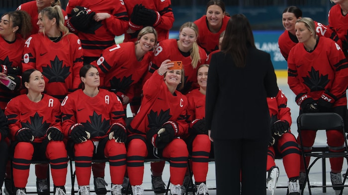 Une hockeyeuse prend un égoportrait avec son téléphone pendant que ses coéquipières sont placées pour la photo d'équipe.