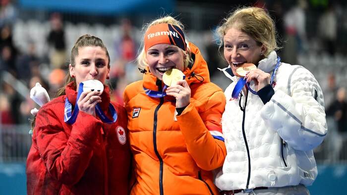 Trois femmes mordent leur médaille en souriant.