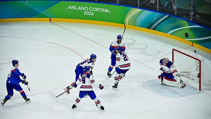 Un joueur de hockey marque un but devant des défenseurs adverses.