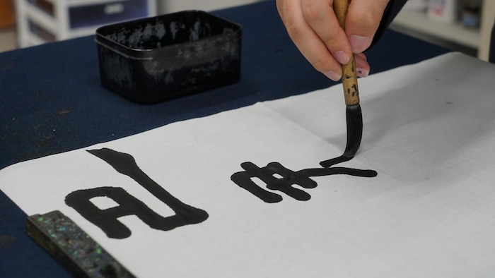 Une main s'applique à l'écriture de kanjis à l'aide d'un pinceau et d'encre.