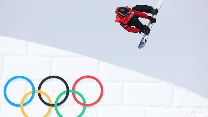 Un planchiste vole dans les airs et agrippe sa planche avec ses mains pendant une épreuve olympique.