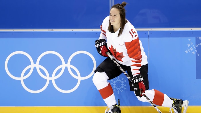 Une hockeyeuse se penche, le dos collé sur la bande.