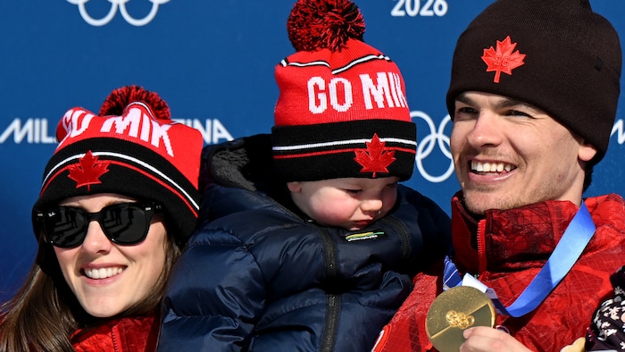 Mikaël Kingsbury avec sa partenaire et son fils aux Jeux de Milan-Cortina, sa médaille d'or au cou, après sa victoire à l’épreuve de bosses en parallèle. 